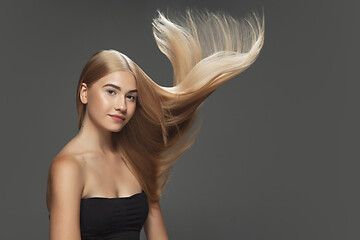 Image showing Beautiful model with long smooth, flying blonde hair isolated on dark studio background.