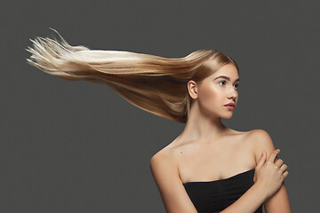 Image showing Beautiful model with long smooth, flying blonde hair isolated on dark studio background.