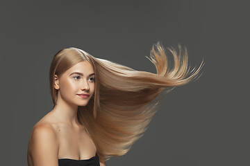 Image showing Beautiful model with long smooth, flying blonde hair isolated on dark studio background.