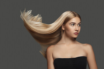 Image showing Beautiful model with long smooth, flying blonde hair isolated on dark studio background.