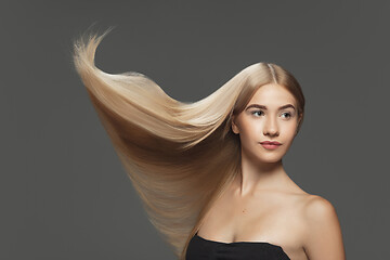 Image showing Beautiful model with long smooth, flying blonde hair isolated on dark studio background.