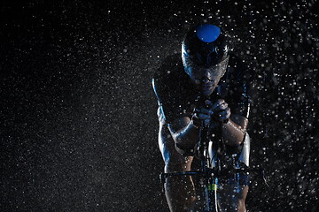 Image showing triathlon athlete riding bike fast on rainy night