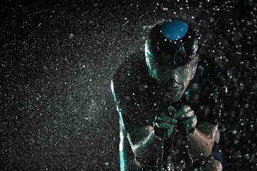 Image showing triathlon athlete riding bike fast on rainy night