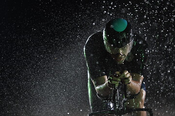 Image showing triathlon athlete riding bike fast on rainy night