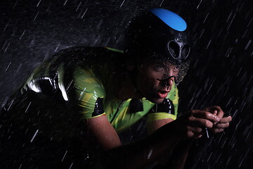 Image showing triathlon athlete riding bike fast on rainy night