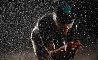 Image showing triathlon athlete riding bike fast on rainy night