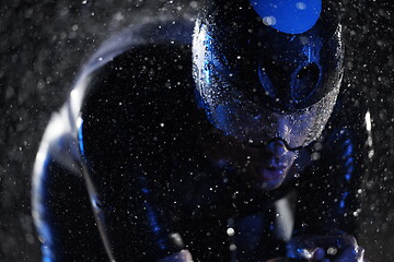 Image showing triathlon athlete riding bike fast on rainy night