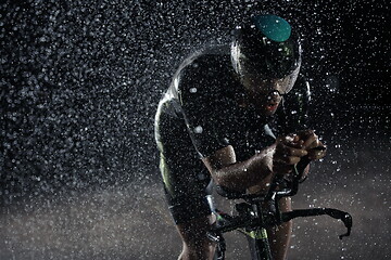 Image showing triathlon athlete riding bike fast on rainy night