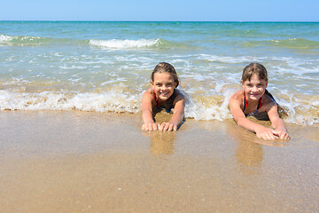 Image showing Girls lie on the sand of the sea coast and happily look at the frame