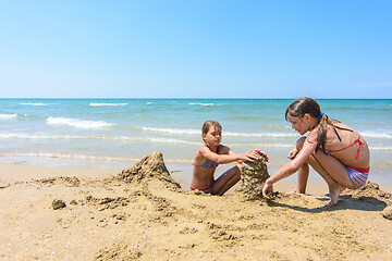 Image showing Two girls play in the sand on the beach of the sea coast