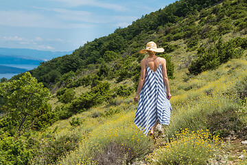 Image showing Young woman wearing striped summer dress and straw hat walking among super bloom of wildflowers, relaxing while enjoing beautiful nature of of Adriatic sea coastal nature of Croatia