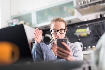 Image showing Stay at home and social distancing. Woman in her casual home clothing working remotly from kitchen dining table. Video chatting using social media with friend, family, business clients or partners