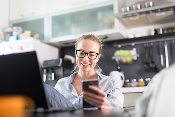 Image showing Stay at home and social distancing. Woman in her casual home clothing working remotly from kitchen dining table. Video chatting using social media with friend, family, business clients or partners