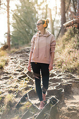 Image showing Active sporty woman listening to the music while hiking in autumn fall forest. Female jogger training outdoor. Healthy lifestyle image of young caucasian woman walking on hiking trail in nature