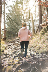 Image showing Rear view of active sporty woman listening to the music while running in autumn fall forest. Female runner training outdoor. Healthy lifestyle image of young caucasian woman jogging outside
