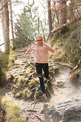 Image showing Active sporty woman running in autumn fall forest jumping over the roots on the path. Healthy lifestyle image of young active caucasian woman jogging outside in nature