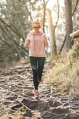 Image showing Active sporty woman listening to the music while running in autumn fall forest. Female runner training outdoor. Healthy lifestyle image of young caucasian woman jogging outside