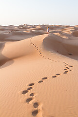 Image showing Blonde female Caucasian traveler leaving footprints in sand dunes when walking in dessert in Oman