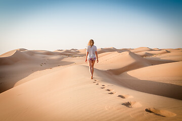 Image showing Blonde female Caucasian traveler leaving footprints in sand dunes when walking in dessert in Oman