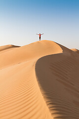Image showing Male traveler standing on the top of dune, arms up to the sky, while traveling sand dessert in Oman.