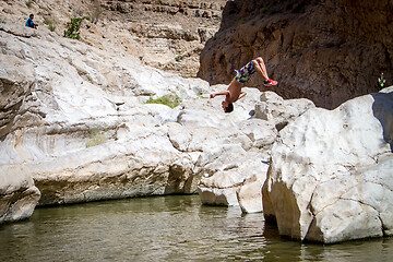 Image showing Sporty guy doing backflip off cliff into lake in an oasis in middle of Oman desert