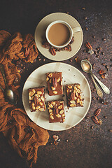 Image showing Chocolate cake with caramel frosting, pecans and hot coffee, on rustic background. Freshly baked