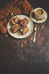 Image showing The square pieces of delicious caramel cake with peanuts and brazil nuts served with milk coffee