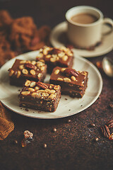 Image showing Chocolate cake with caramel frosting, pecans and hot coffee, on rustic background. Freshly baked