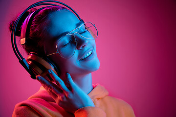 Image showing Fashion pretty woman with headphones listening to music over neon background