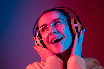 Image showing Fashion pretty woman with headphones listening to music over neon background