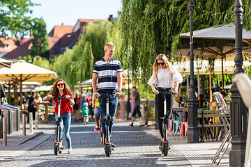 Image showing Trendy fashinable group of friends riding public rental electric scooters in urban city environment. New eco-friendly modern public city transport in Ljubljana, Slovenia