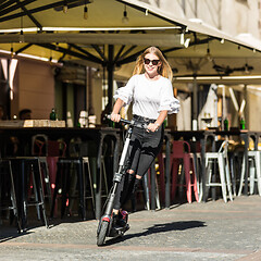 Image showing Trendy fashinable teenager girls riding public rental electric scooters in urban city environment. New eco-friendly modern public city transport in Ljubljana, Slovenia