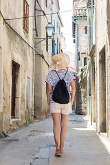 Image showing Rear view of beautiful blonde young female traveler wearing straw sun hat sightseeing and enjoying summer vacation in an old traditional costal town at Adriatic cost, Croatia