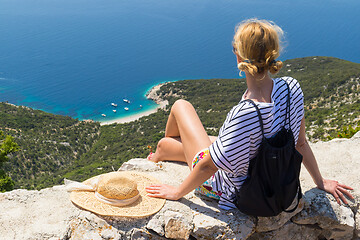 Image showing Active sporty woman on summer vacations sitting on old stone wall at Lubenice village, wearing straw hat and beach backpack enjoying beautiful coastal view of Cres island, Croatia