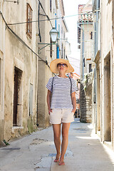 Image showing Beautiful blonde young female traveler wearing straw sun hat sightseeing and enjoying summer vacation in an old traditional costal town at Adriatic cost, Croatia