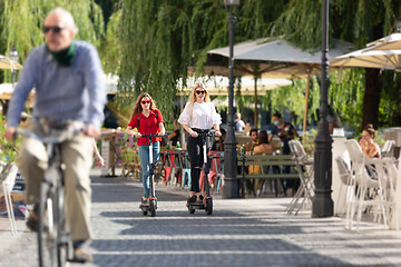 Image showing Trendy fashinable teenager girls riding public rental electric scooters in urban city environment. New eco-friendly modern public city transport in Ljubljana, Slovenia