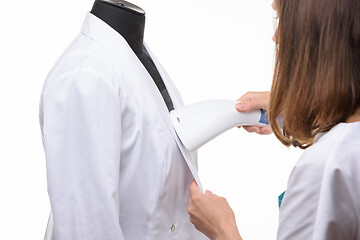 Image showing Girl handles medical clothing by steamer on a white background