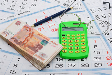 Image showing A bundle of money, calculator, glasses and a ballpoint pen lies on the background from the calendar