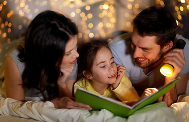 Image showing happy family reading book in bed at night at home