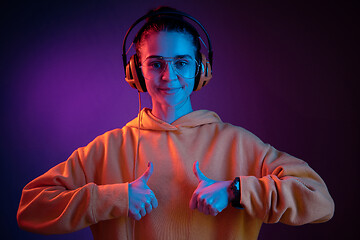 Image showing Fashion pretty woman with headphones listening to music over neon background