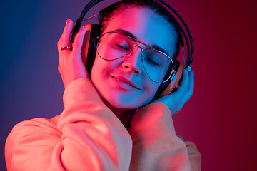 Image showing Fashion pretty woman with headphones listening to music over neon background