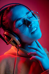 Image showing Fashion pretty woman with headphones listening to music over neon background