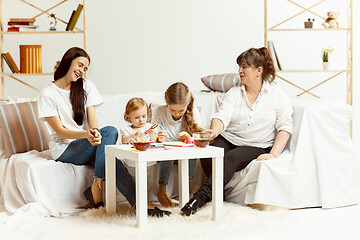 Image showing Little girls, attractive young mother and charming grandmother are sitting at home