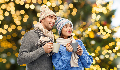 Image showing happy couple with mugs over christmas lights