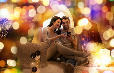 Image showing happy couple with smartphone in kids tent at home