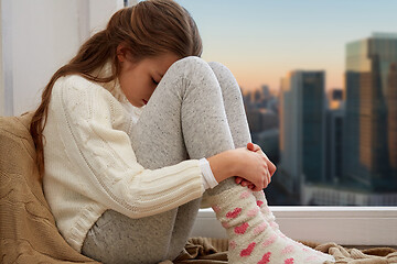 Image showing sad girl sitting on sill at home window over city