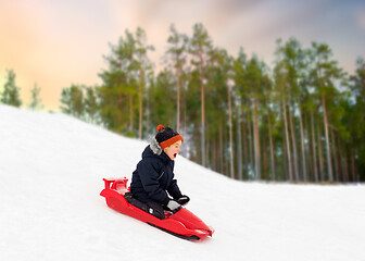 Image showing happy boy sliding on sled down snow hill in winter