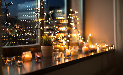 Image showing candles burning on window sill with garland lights