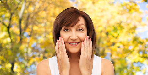 Image showing smiling senior woman touching her face in autumn