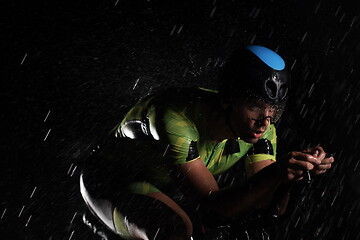 Image showing triathlon athlete riding bike fast on rainy night